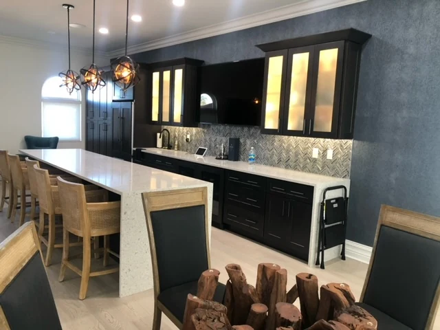 Full view of an entertainment bar with dark illuminated cabinets and light waterfall countertops