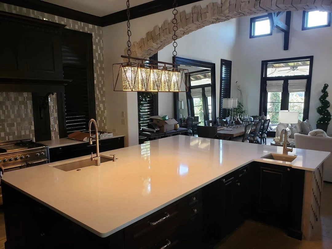 Large light kitchen island with two sinks, dark cabinetry, and a stone arch beyond