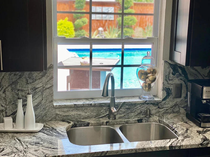 Double-bowl kitchen sink surrounded by patterned stone countertops and matching window ledge