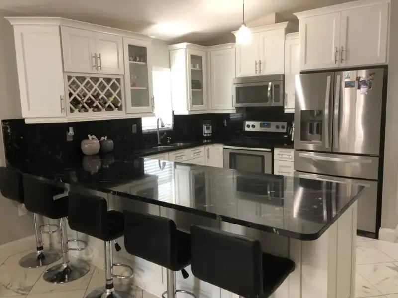 White kitchen cabinetry and wine storage above a polished dark countertop with peninsula seating